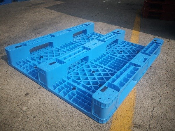 A single blue plastic pallet with a grid - like structure and reinforced sections, placed on a concrete surface with a yellow line, exemplifying the sturdy and durable nature of plastic pallets.
