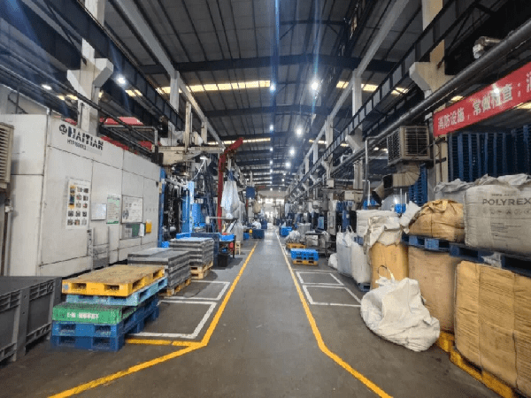 A bustling factory interior with machinery, various plastic pallets in colors like blue and yellow, and industrial materials. It reflects the production scale of top 10 plastic pallet manufacturers in Ecuador.