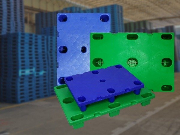 A display of blue and green plastic pallets with distinct designs, set against a warehouse backdrop. This showcases the variety and quality from top 10 plastic pallet manufacturers in Mexico.