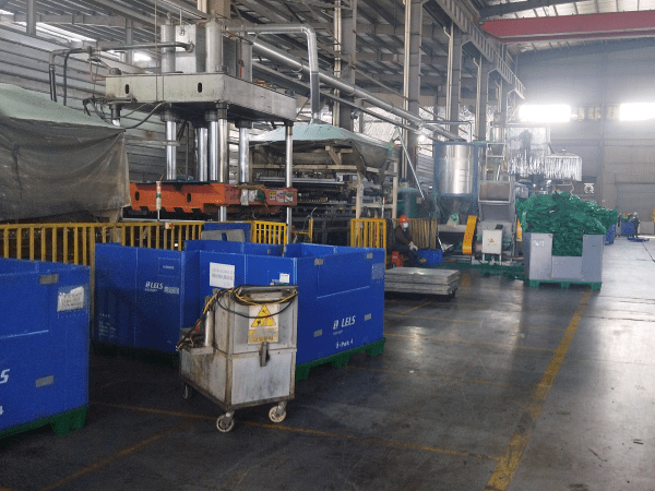 A busy factory with large machinery and stacks of blue plastic containers, reflecting the production capacity of top 10 plastic pallet manufacturers in Russia.