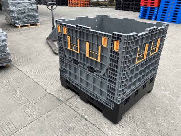There is a foldable plastic pallet box on the factory floor. There is an orange valve on the box, which is used to open the small door on the side panel of the box.