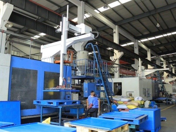 An industrial factory with machinery and blue plastic pallets. In Australia, the standard pallet size is 1165 mm x 1165 mm, commonly made of plastic or wood, with an average height of 150 mm.