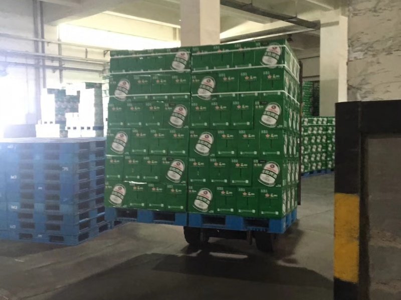 Green beverage boxes stacked on a blue pallet, transported by a cart in a warehouse.