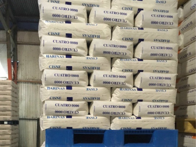 Interlocking pattern stacks of “CISNE” flour bags on a blue plastic pallet in a warehouse.